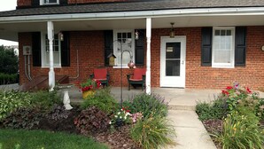 A brick house with a front porch, two red chairs, and a white door. - Spruce Lane Lodge and Cottages (Lancaster)