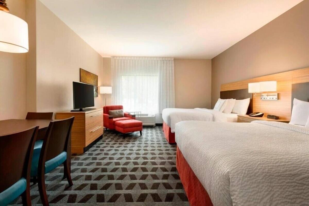 Une chambre d’hôtel avec un lit, un bureau, une chaise, une télévision et une fenêtre avec des rideaux.