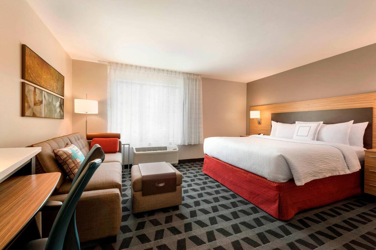 Une chambre d’hôtel avec un lit, un bureau, une chaise, une petite table et une fenêtre avec des rideaux.