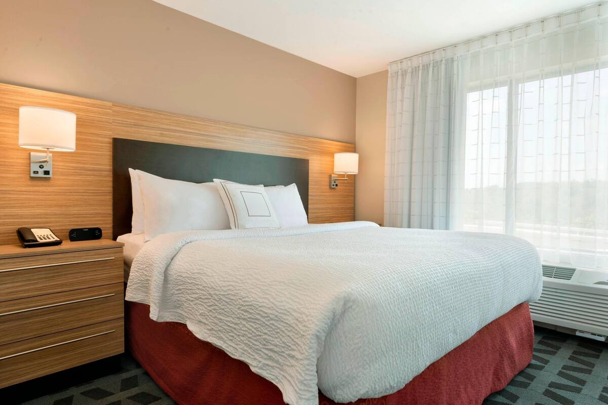 Une chambre d’hôtel avec un lit, des lampes de chevet, un téléphone et une fenêtre avec des rideaux.