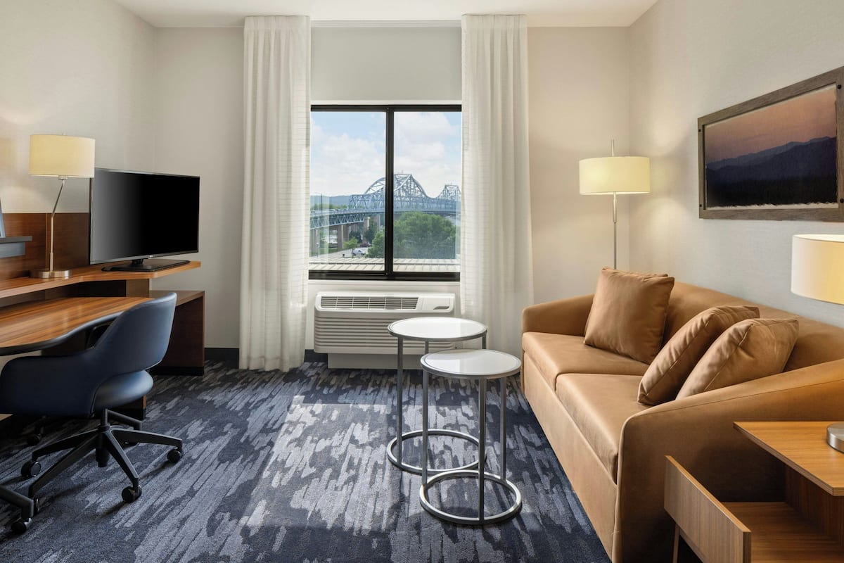 Ein Hotelzimmer mit großem Fenster, Fernseher, Schreibtisch, Stuhl, Sofa und Lampe.