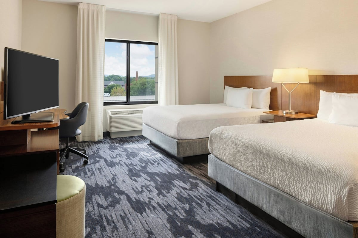 Ein Hotelzimmer mit zwei Betten, einem Schreibtisch mit Computer, einem Fernseher und Blick ins Freie.
