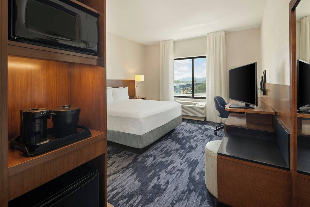 Ein Hotelzimmer mit einem Bett, einem Schreibtisch mit Computer, einem Fernseher, einer Kaffeemaschine und einem Fenster mit Blick auf die Stadt.