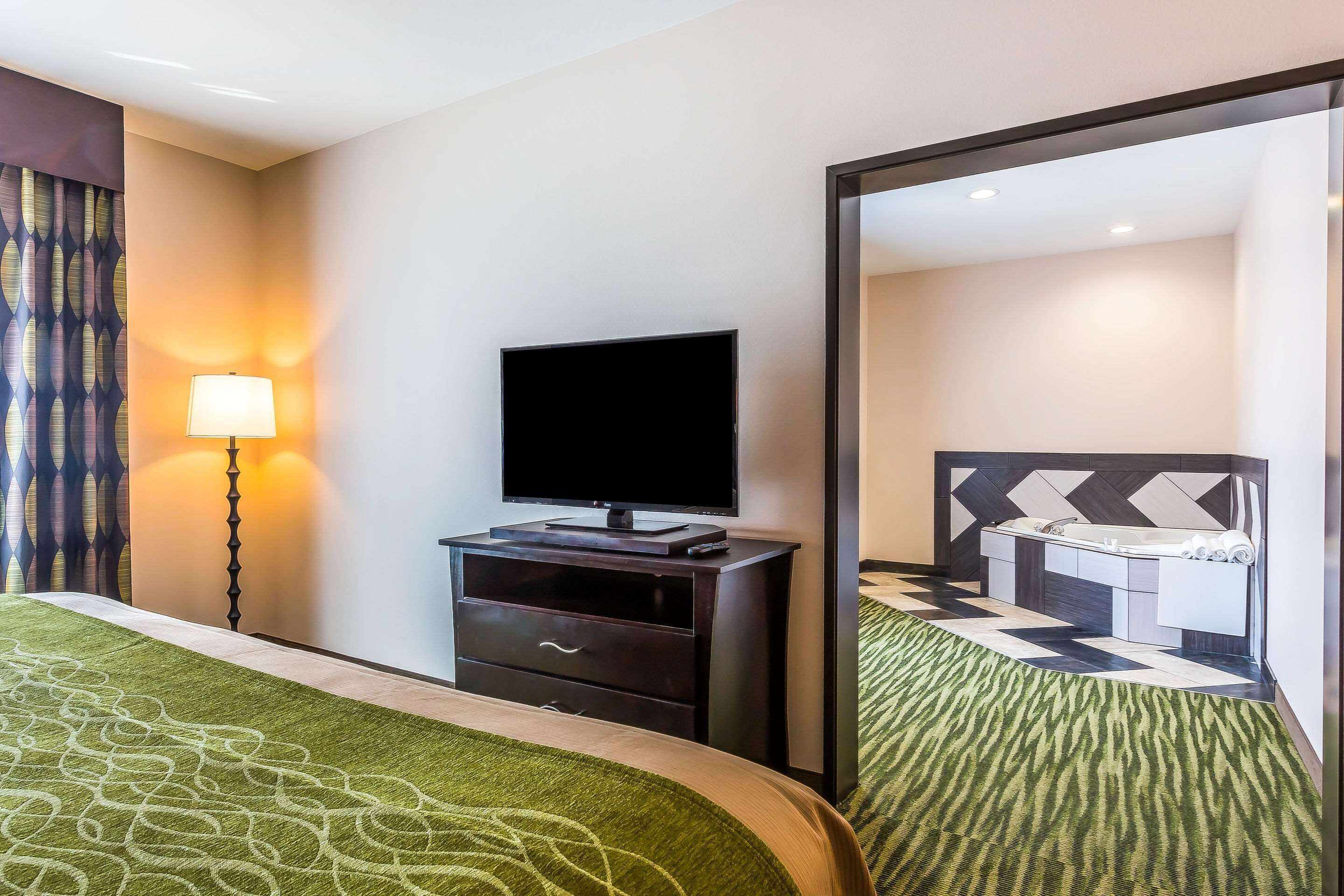 Habitación de hotel con cama, televisor de pantalla plana, escritorio con cajones, lámpara y un espejo grande.