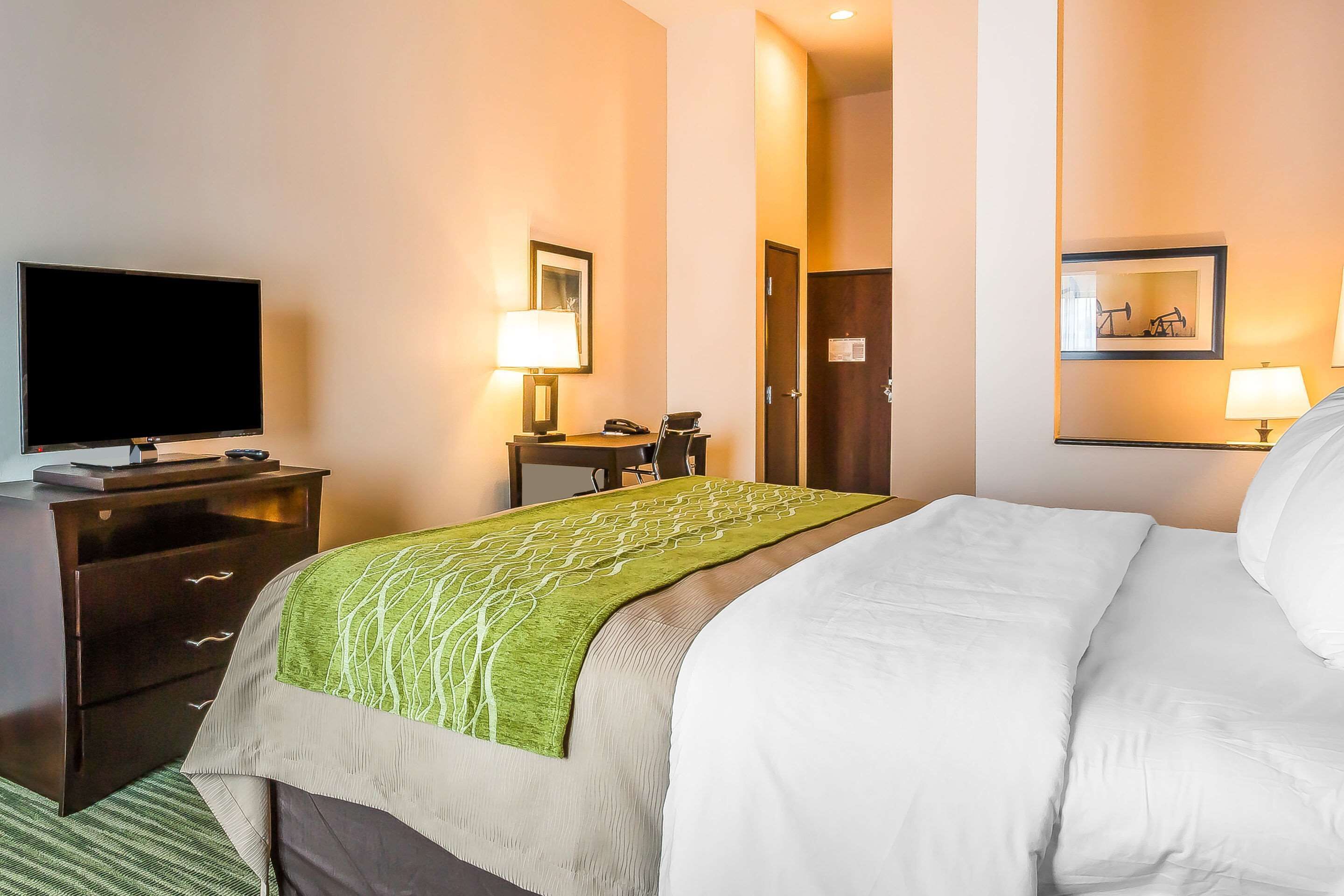 Een hotelkamer met een bed, een televisie, een bureau met lamp en een deur.