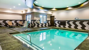 Une piscine intérieure avec des lignes de démarcation claires pour les couloirs, un plafond orné d’un luminaire circulaire et un mur décoré d’un motif en chevrons.