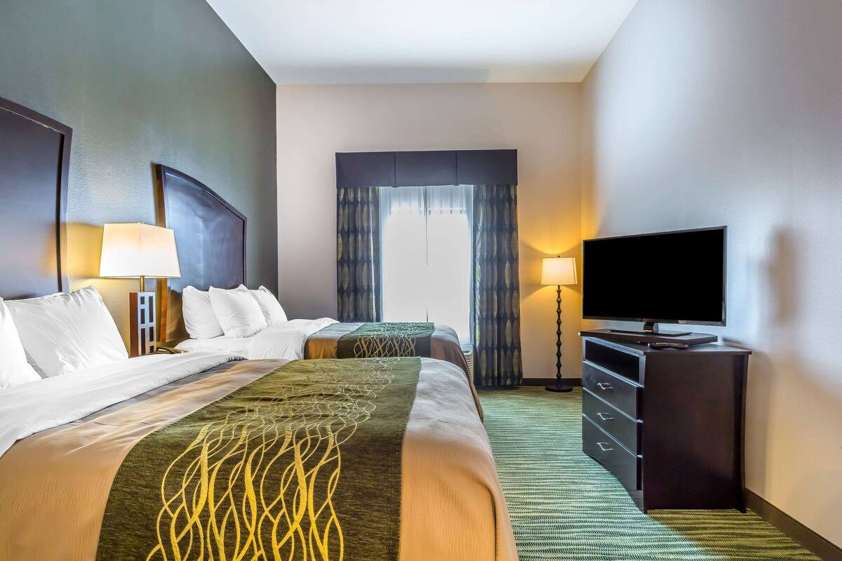 Una habitación de hotel con dos camas, un televisor de pantalla plana, un aparador y una ventana con cortinas.