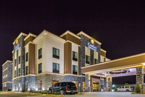 Un Comfort Inn con fachada de piedra, varias entradas y un estacionamiento con vehículos.