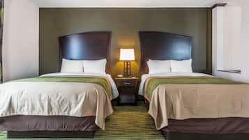 Quarto de hotel com duas camas, mesa de cabeceira com abajur e tapete verde.