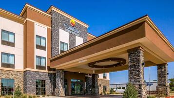 A Comfort Inn & Suites hotel with a stone facade, a covered entrance, and a clear blue sky.