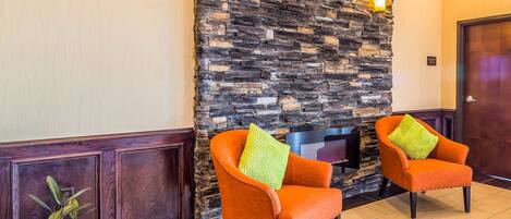 Zona de recepción con pared de piedra, dos sillones naranjas con cojines verdes, una planta en maceta y un panel de pared de madera.