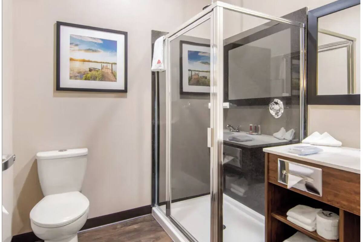 Un bany modern amb plat de dutxa tancat per vidre, vàter blanc, un lavabo amb mirall i quadres al mur.