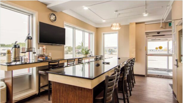 A modern kitchen with a central island, bar stools, and a flat-screen TV mounted on the wall. - Albertan Inn (Fox Creek)