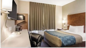 A hotel room with a bed, a desk with a telephone, a chair, a television, and a window with curtains. - Albertan Inn (Fox Creek)
