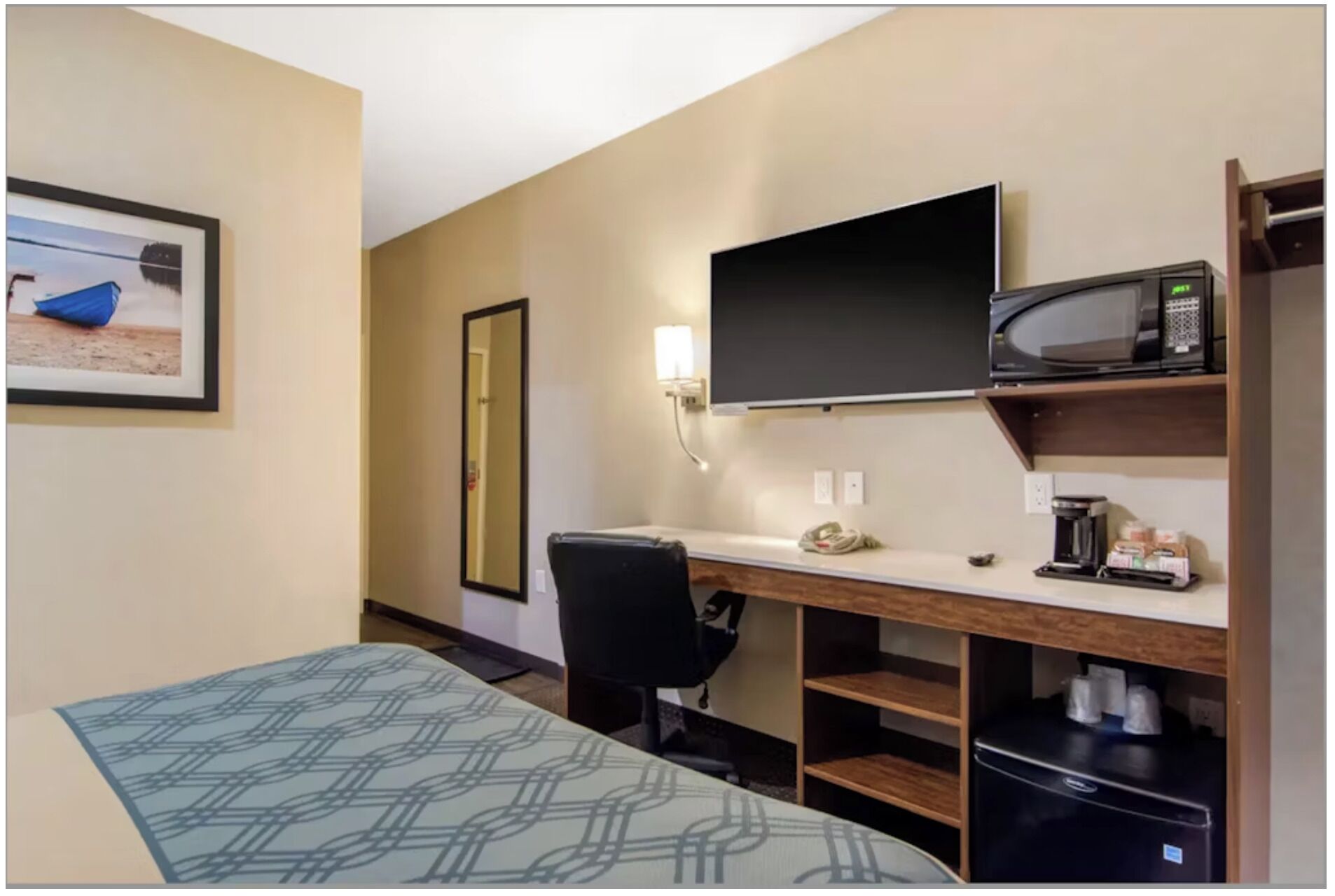 Ein Hotelzimmer mit einem Bett, einem Schreibtisch mit Computer, einem Flachbildfernseher, einer Mikrowelle und einer Kaffeemaschine.