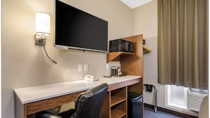 A hotel room with a desk, chair, television, coffee maker, and a trash bin. - Albertan Inn (Fox Creek)