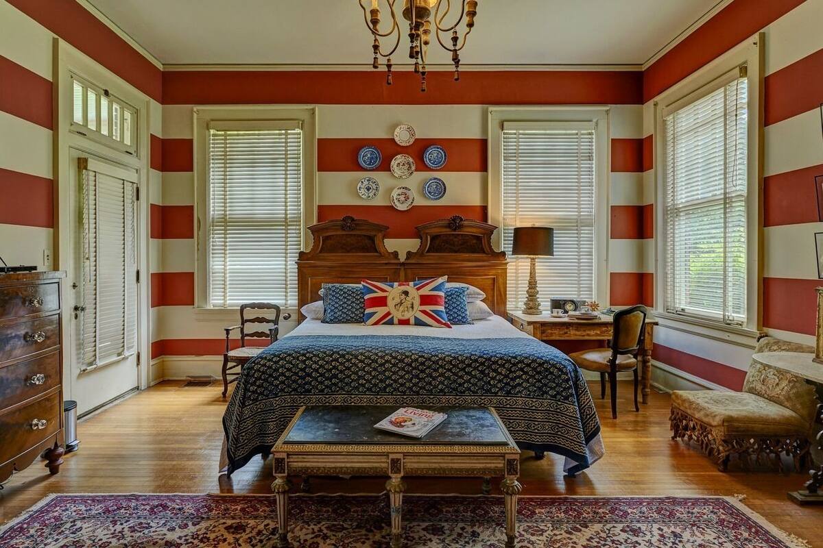 A bedroom with a large bed, a wooden dresser, a desk, and a chandelier.