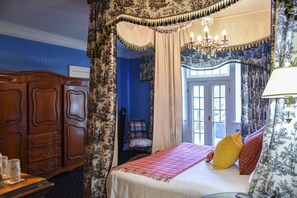 A bedroom with a four-poster bed, a wooden wardrobe, and a chair. - The English Merchant's Inn (Waxahachie)