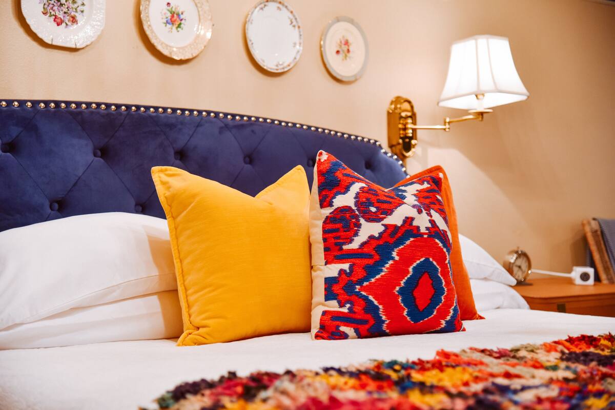 A bed with a tufted headboard, two pillows, a patterned rug, and wall-mounted plates and a lamp.