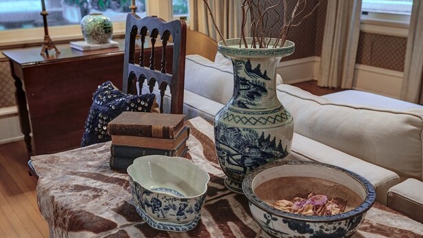 A table with a patterned tablecloth, a vase with branches, a bowl with food, and a decorative chair. - The English Merchant's Inn (Waxahachie)