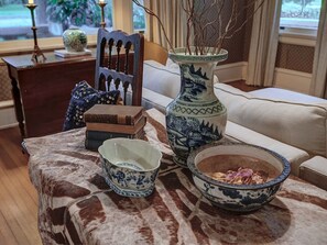 Een tafel met een tafelkleed met patroon, een vaas met takken, een schaal met eten, en een decoratieve stoel.