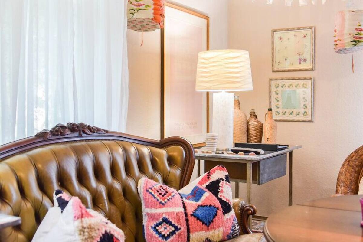 A cozy living room with a brown leather sofa, patterned cushions, a small table with a lamp, and a mirror.