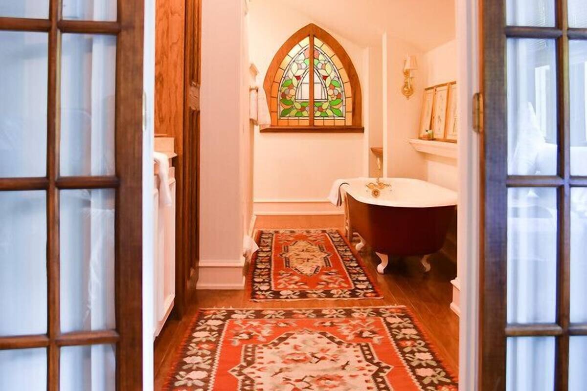 A bathroom with a wooden cabinet, a round mirror, a stained glass window, and a red patterned rug.