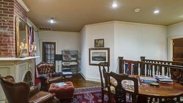 A spacious living room with a fireplace, a dining area with a wooden table and chairs, and a red patterned rug.