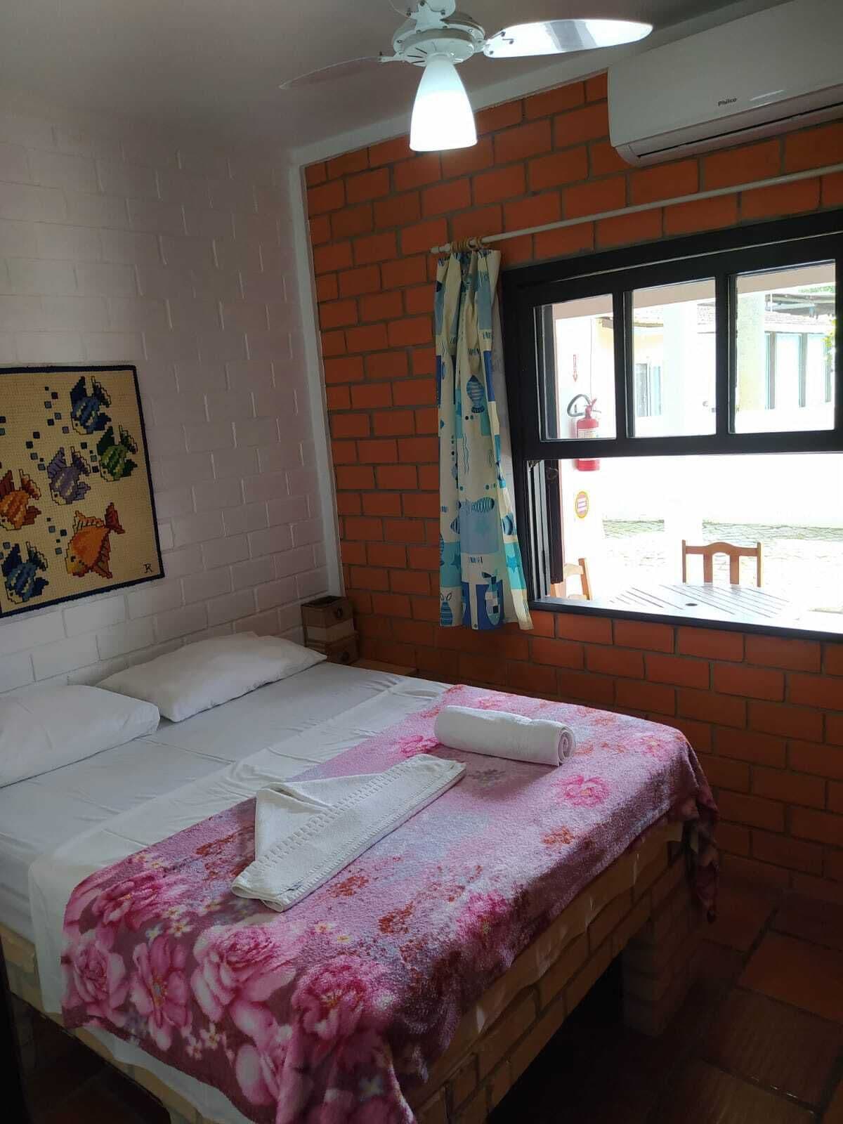 A bedroom with a bed, a window with a view, a ceiling fan, and a wall-mounted air conditioner.