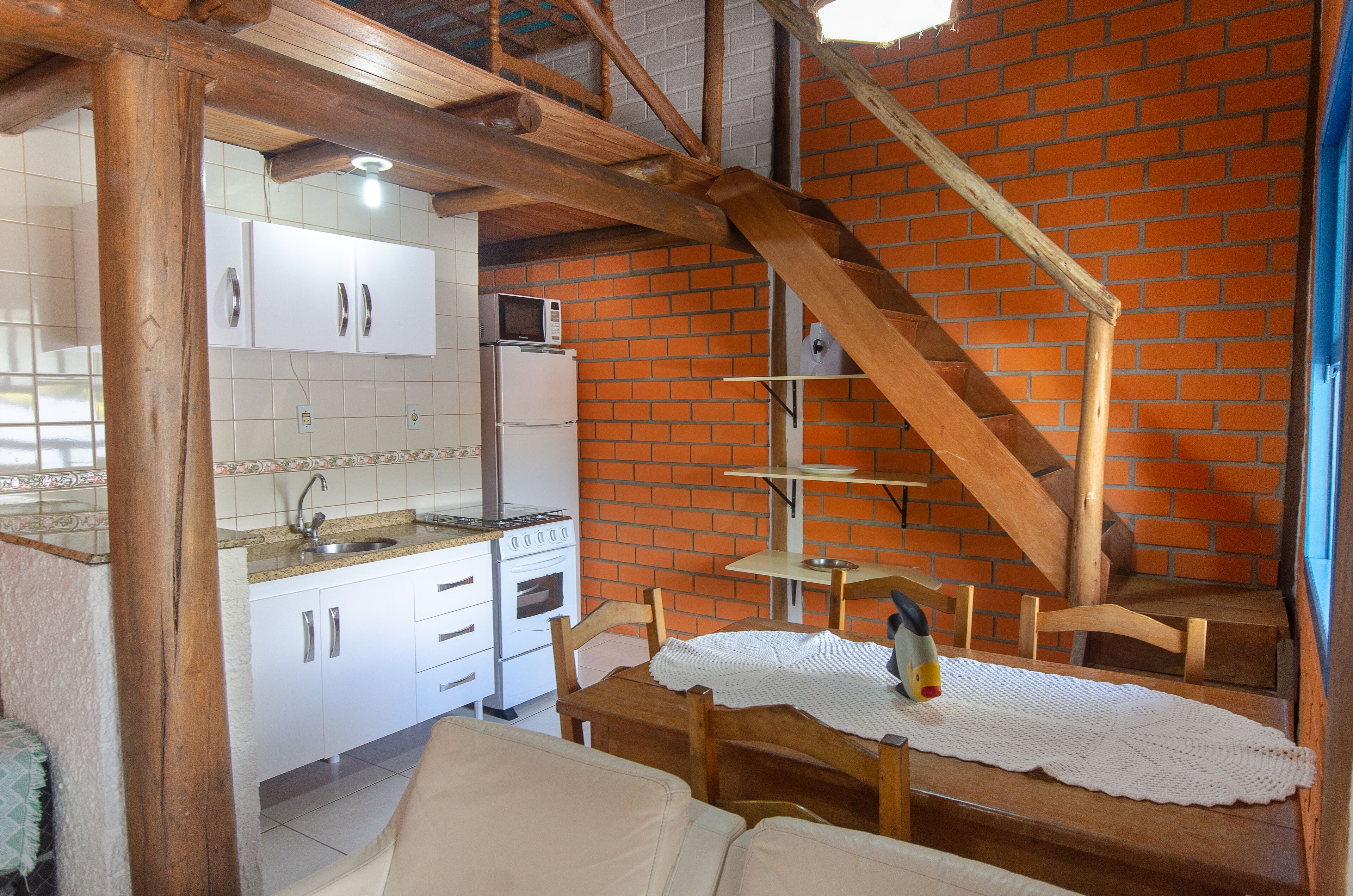 A kitchen with white cabinets, a microwave, and a refrigerator. There is a wooden staircase leading to a balcony.