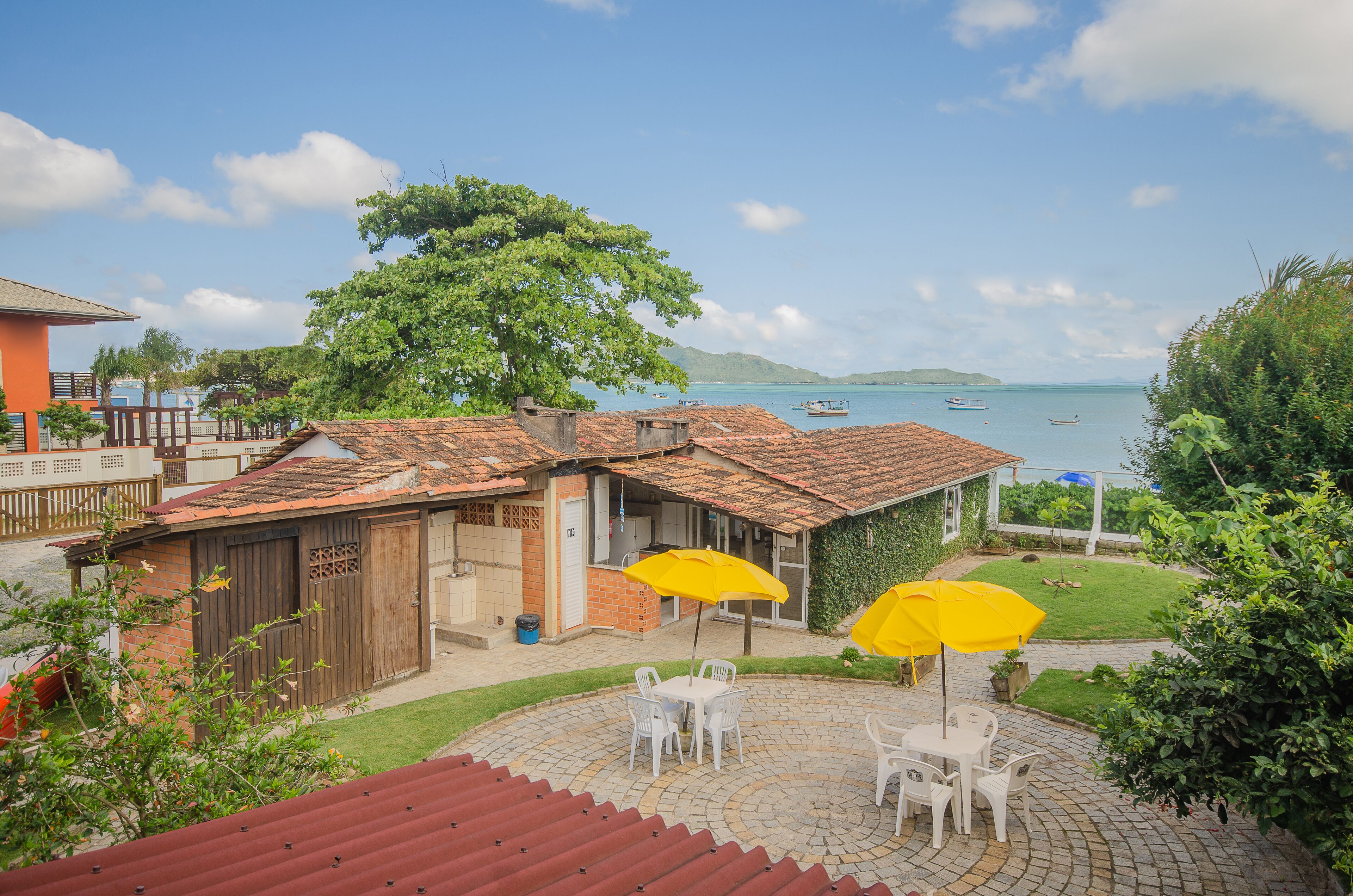 A patio with white chairs and yellow umbrellas, overlooking a beach with boats and a clear sky.