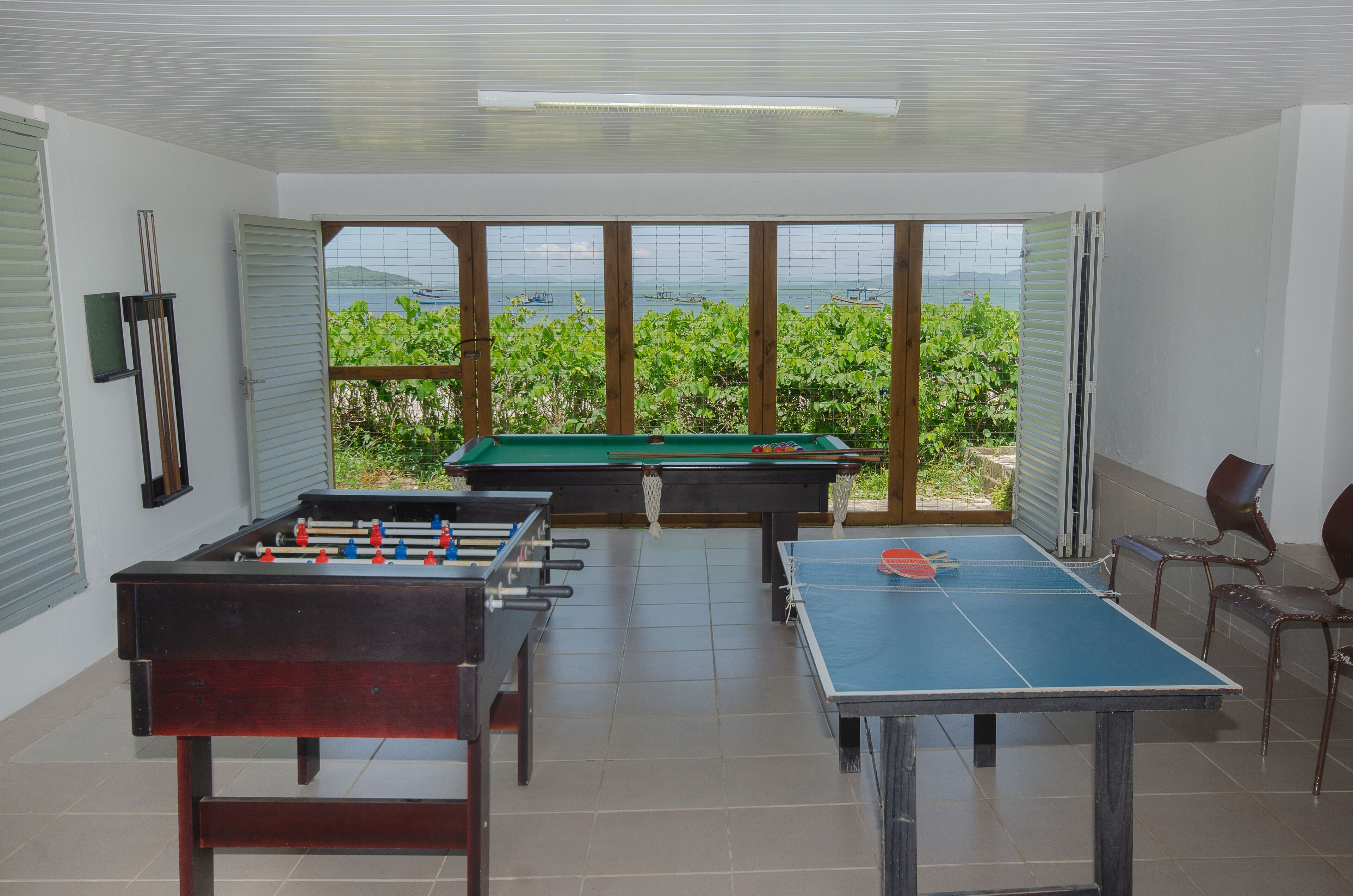 Uma sala com mesa de pebolim, mesa de sinuca e mesa de bilhar.