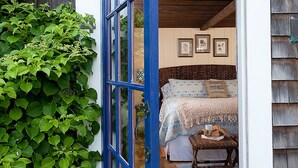 A bedroom with a bed, a small table with a cup and a book, and a wall with framed pictures.