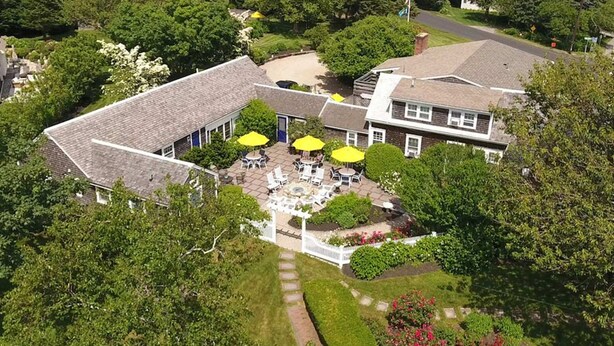 An aerial view of a property with a large house, a patio with outdoor seating, and a view of the sea.