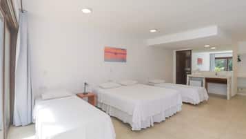 A hotel room with three single beds, a desk with a chair, and a small kitchenette.