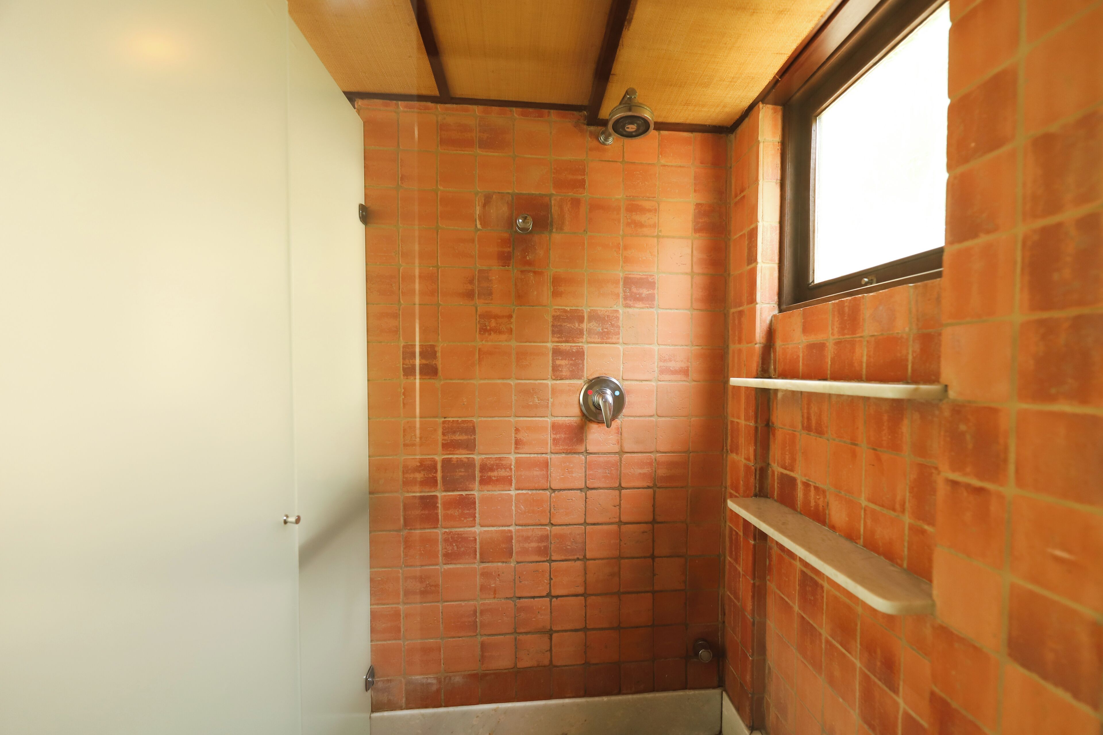 Une douche avec un mur carrelé, une fenêtre et une porte blanche.