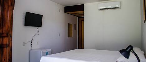 A bedroom with a bed, a desk with a lamp, a television, an air conditioner, and a wardrobe.