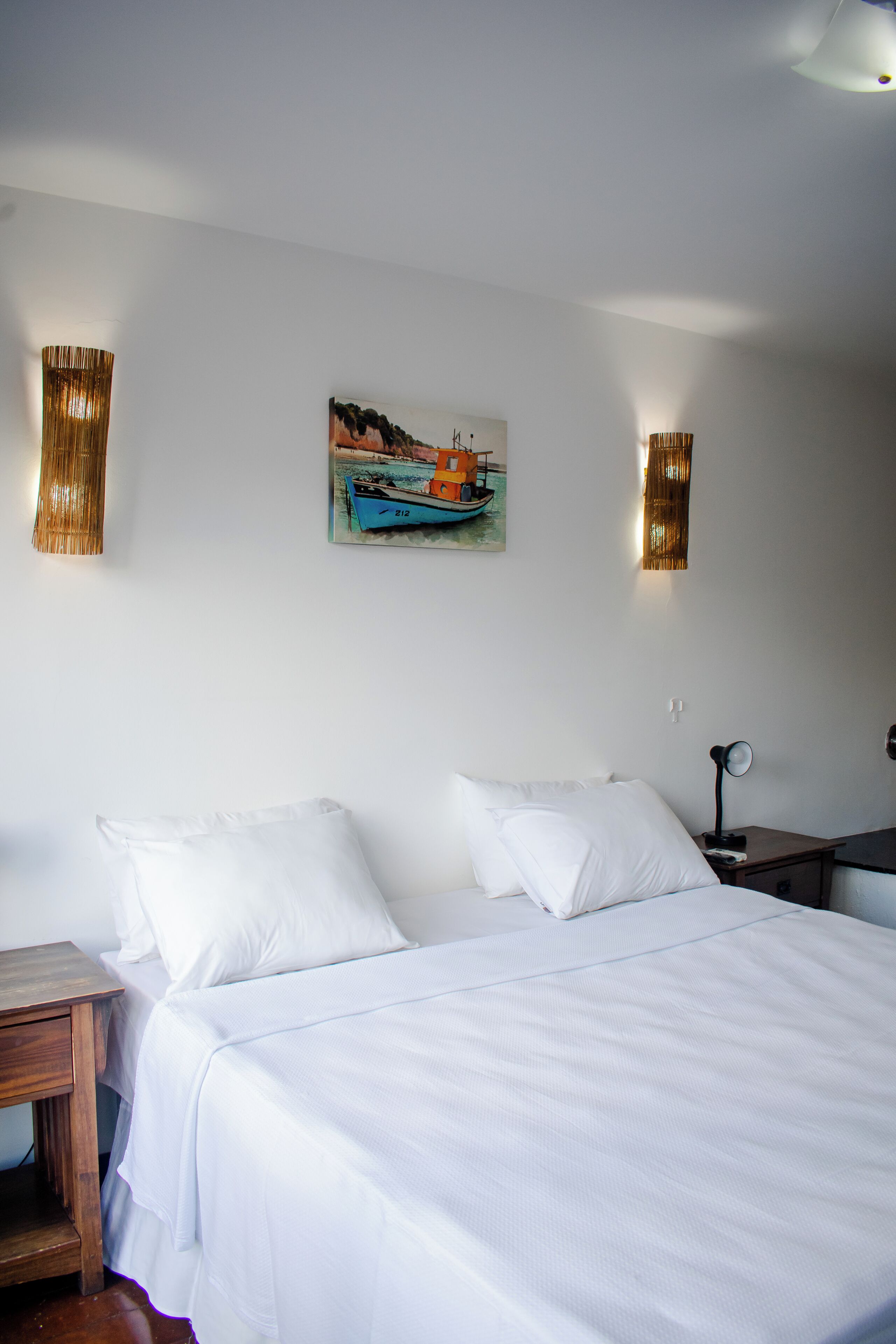 Una cama bien hecha con sábanas blancas, una mesita de noche pequeña y un cuadro colgado en la pared de un barco.