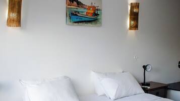 Una cama bien hecha con sábanas blancas, una mesita de noche pequeña y un cuadro colgado en la pared de un barco.