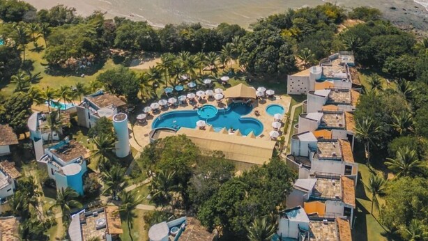 Vista aérea de un complejo turístico con varias piscinas, una playa y exuberante vegetación.