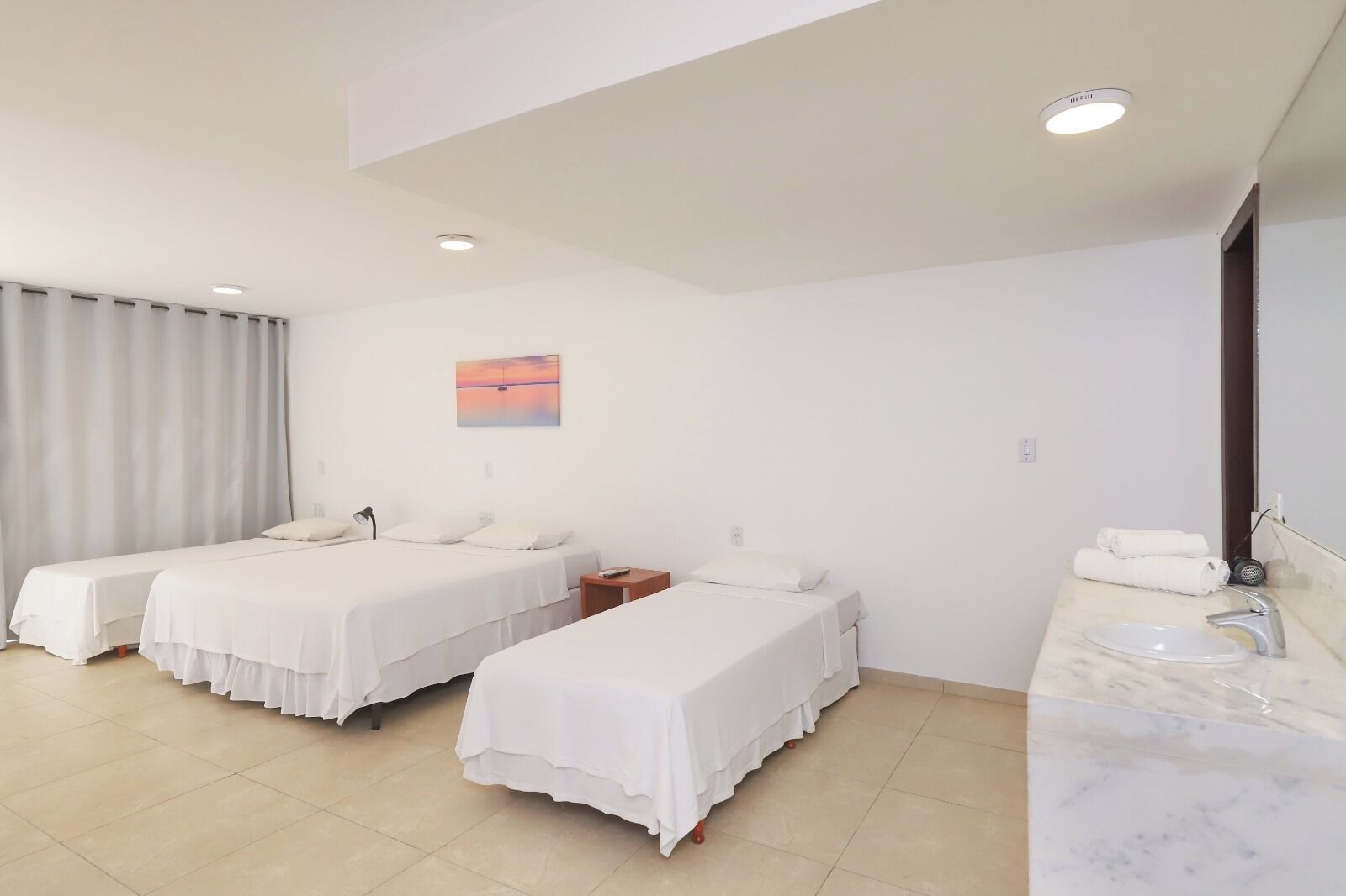 A hotel room with two single beds, a bathroom with a sink and mirror, and a painting on the wall.