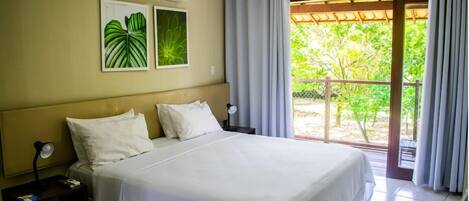 A hotel room with a bed, a nightstand, an air conditioner, and a view of greenery through a sliding door.