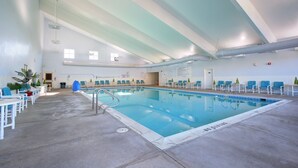 An indoor swimming pool with clear water, surrounded by white lounge chairs and tables. - Sea Scape Beach and Golf Villas (Kitty Hawk)