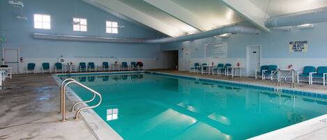 A large indoor swimming pool with clear water, surrounded by blue chairs and a no diving sign.
