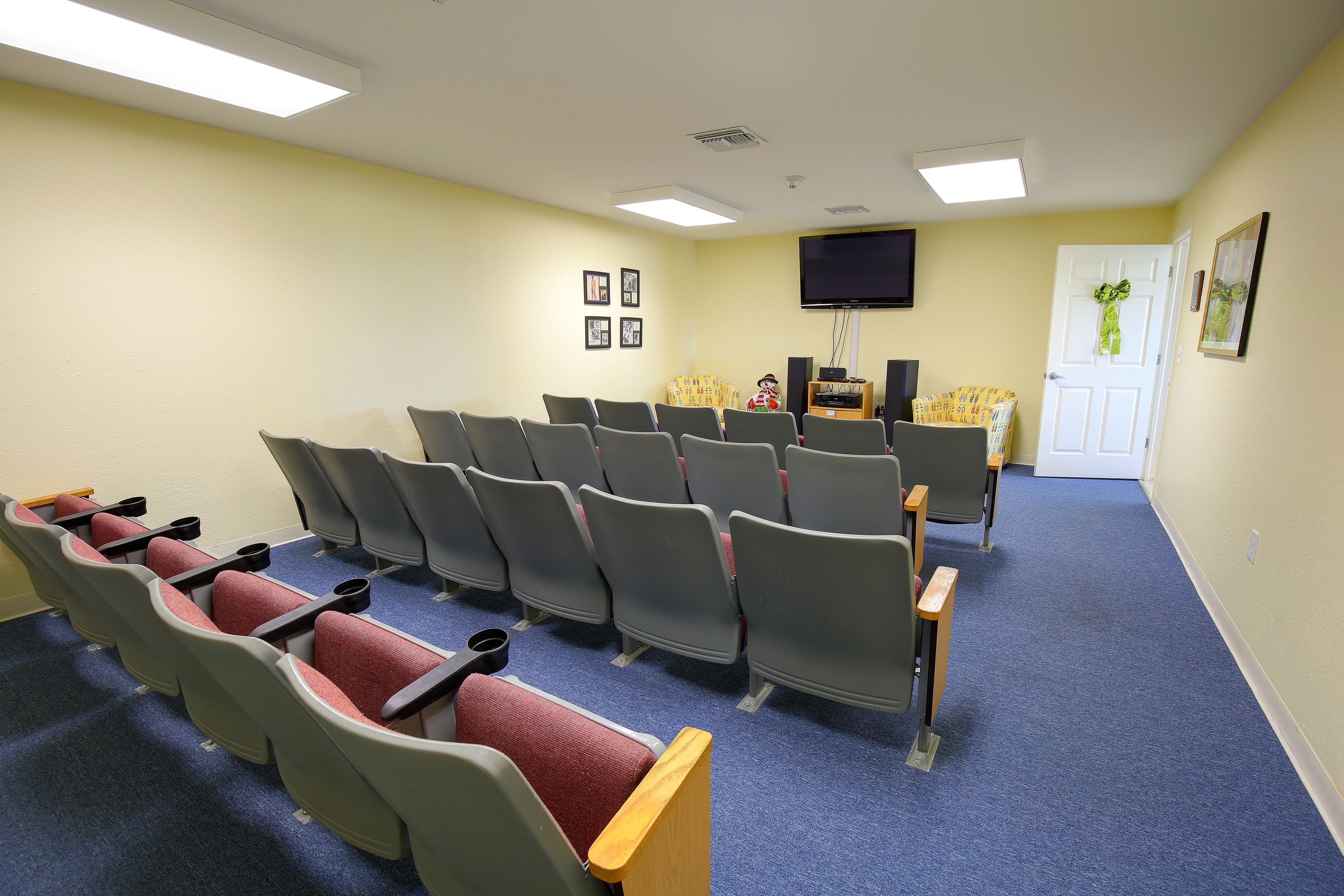 A conference room with rows of chairs, a projector screen, and a door with a green wreath.