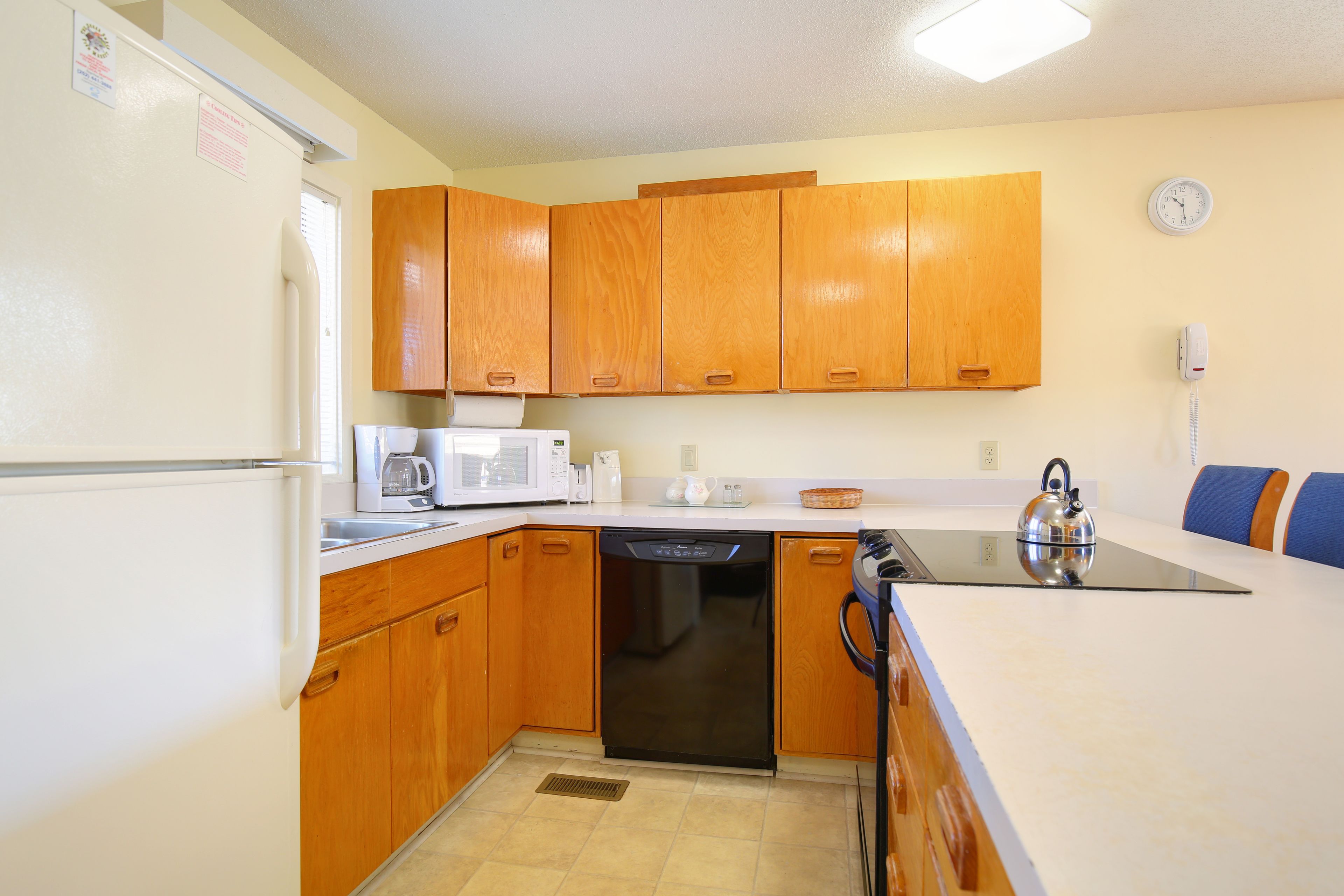A compact kitchen with wooden cabinets, a dishwasher, a microwave, and a kettle on the countertop.