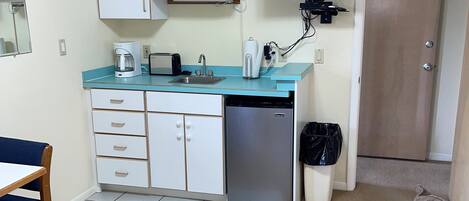 Een compacte keuken met een magnetron, koffiezetapparaat en vaatwasser. Er is een bank en een fauteuil in de woonkamer.