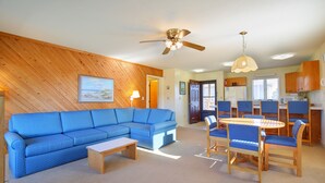 A living room with a blue sofa, a wooden coffee table, and a dining area with a round table and chairs. - Sea Scape Beach and Golf Villas (Kitty Hawk)