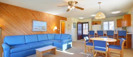 A living room with a blue sofa, a wooden coffee table, and a dining area with a round table and chairs.