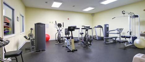 A gym with various exercise machines, a red exercise ball, and a window with a view of a building.